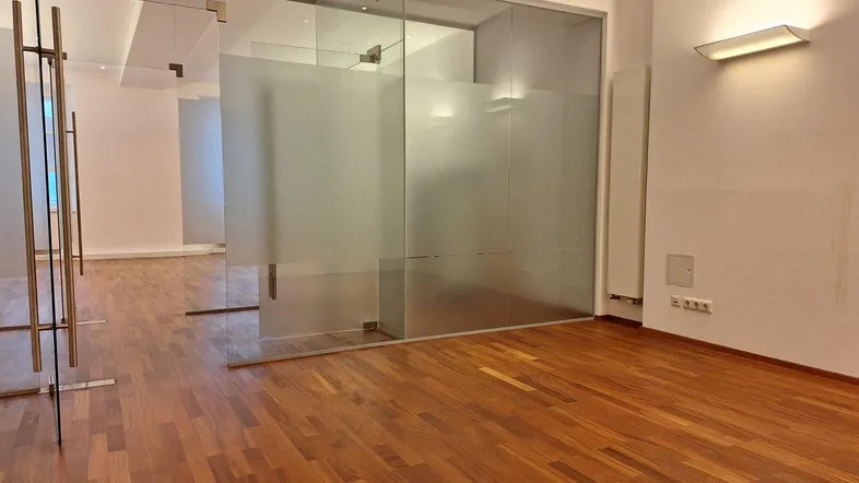 Moderner Büroraum mit Holzboden und Glaswänden, die für Transparenz und Helligkeit sorgen.