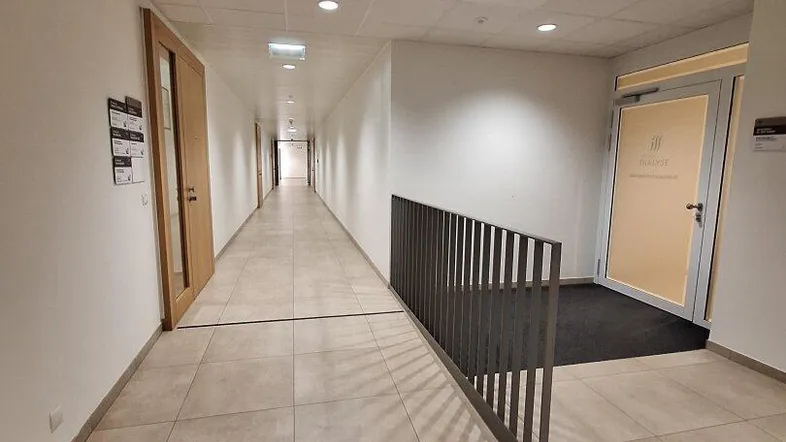 Langer, heller Flur mit beigen Fliesen und Holztüren, der zu verschiedenen Büros führt.