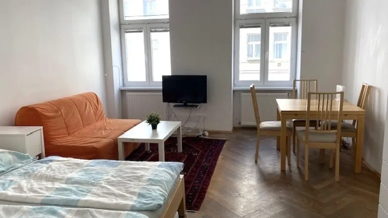 Helles Wohn- und Schlafzimmer mit Parkettboden, Esstisch und gemütlichem Sofa.