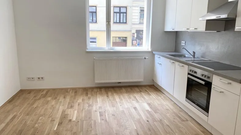 Helle Wohnküche mit moderner Einbauküche, Parkettboden und Blick auf die Straße.