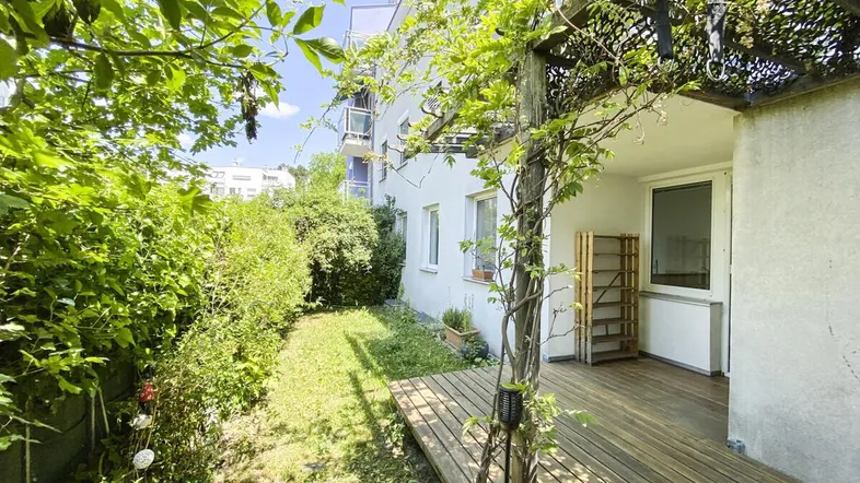 Sonniger Gartenbereich mit Holzterrasse und üppiger Bepflanzung, ideal zum Entspannen im Freien.