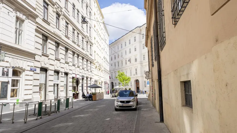 Eine belebte Gasse in der Stadt mit historischen Gebäuden und einem gepflasterten Gehweg.