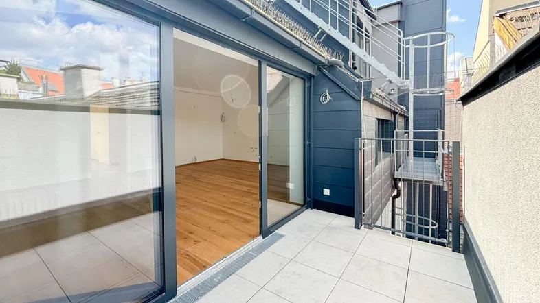 Moderne Dachterrasse mit Fliesenboden und großen Glasschiebetüren, die zum Innenbereich führen.