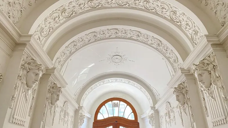 Eindrucksvoller Eingangsbereich mit hohen Decken, kunstvollen Stuckverzierungen und einer eleganten Holztür.