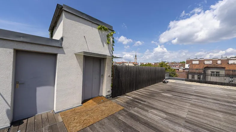 Geräumige Dachterrasse mit Holzboden und weitem Blick über die Stadt unter blauem Himmel.