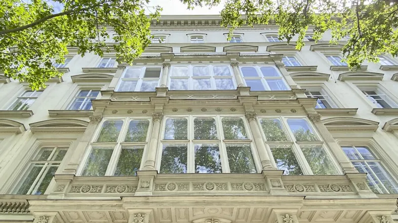 Elegante Fassade eines historischen Gebäudes mit reich verzierten Erkern und grünen Bäumen.