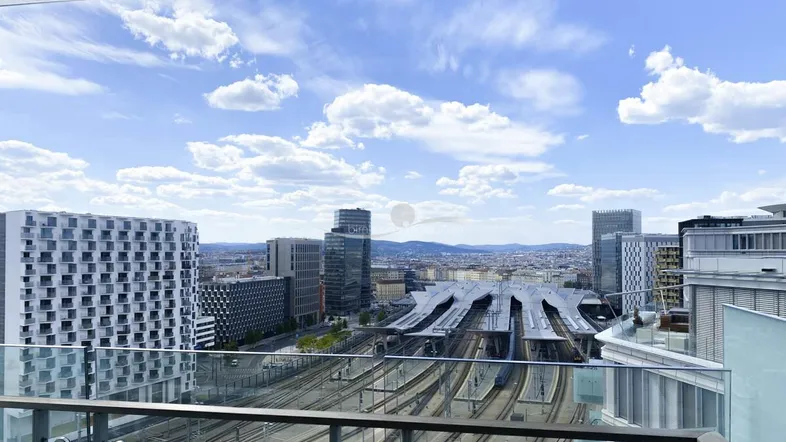 Panoramablick von einem modernen Balkon auf die Stadt und den Hauptbahnhof unter blauem Himmel.