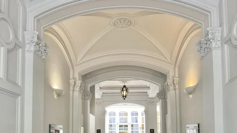 Eleganter Flur mit hohen Decken, Stuckverzierungen und klassischer Beleuchtung in einem historischen Gebäude.