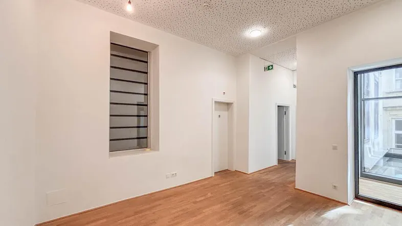 Heller Büroraum mit Holzboden, hohen Decken und einem großen Fenster, das viel Tageslicht hereinlässt.