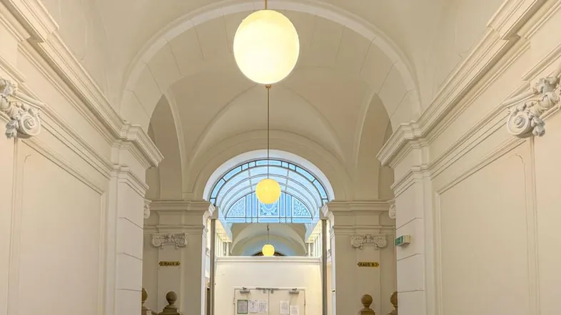 Repräsentativer Flur mit hohen Gewölbedecken, Stuckelementen und großen Kugellampen.