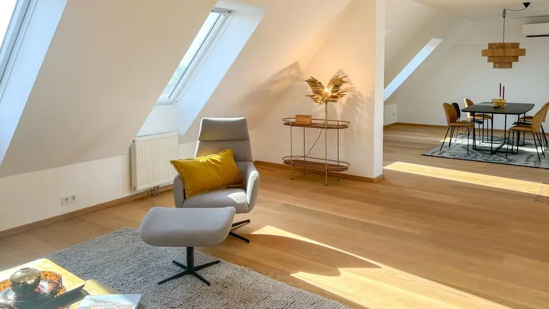 Lichtdurchfluteter Wohn- und Essbereich mit Dachschrägen, Holzboden und moderner Einrichtung.