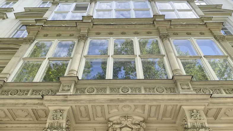 Detailaufnahme einer prunkvollen Fassade mit großen Fenstern und reich verzierten architektonischen Elementen.