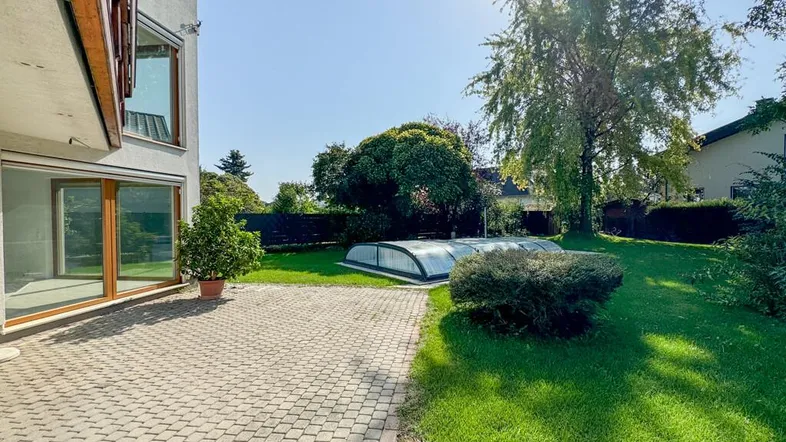 Großer Gartenbereich mit gepflasterter Terrasse, Rasenfläche und einem überdachten Swimmingpool.