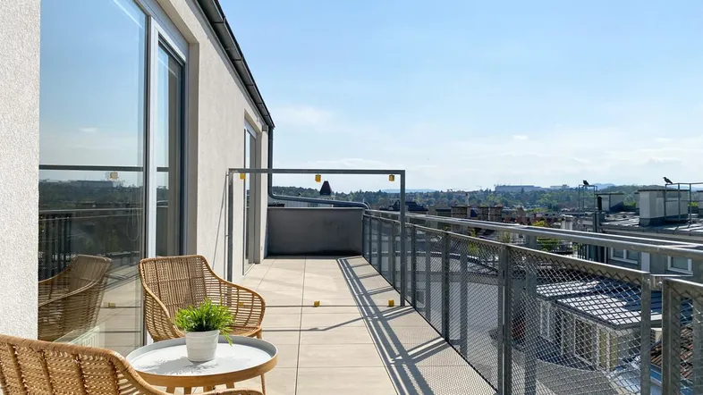 Geräumiger Balkon mit Sitzgelegenheiten und weitem Blick über die Stadt und grüne Hügel.