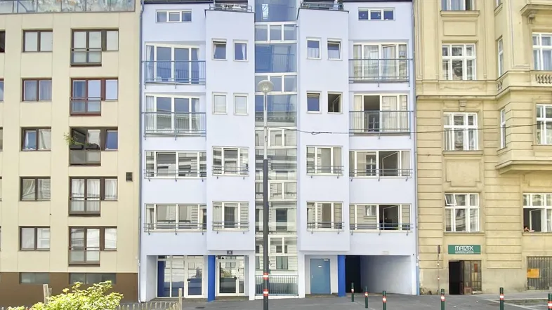Modernes Mehrfamilienhaus mit hellblauer Fassade, vielen Fenstern und Balkonen, umgeben von anderen Gebäuden in urbaner Umgebung.