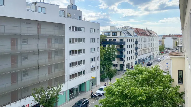 Blick von oben auf eine belebte Stadtstraße mit modernen Gebäuden und viel Grün.