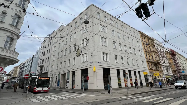 Gebäude an einer belebten Straßenkreuzung in der Stadt mit Straßenbahnen und Passanten.