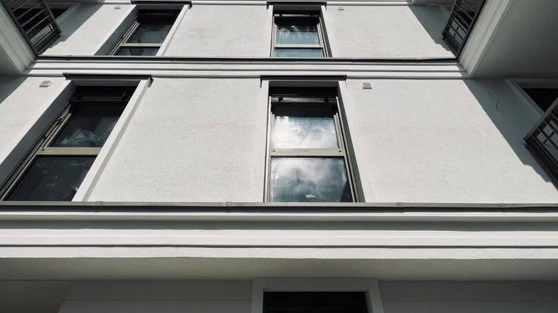 Moderne weiße Fassade eines Neubaus mit mehreren Balkonen und großen Fenstern unter blauem Himmel.