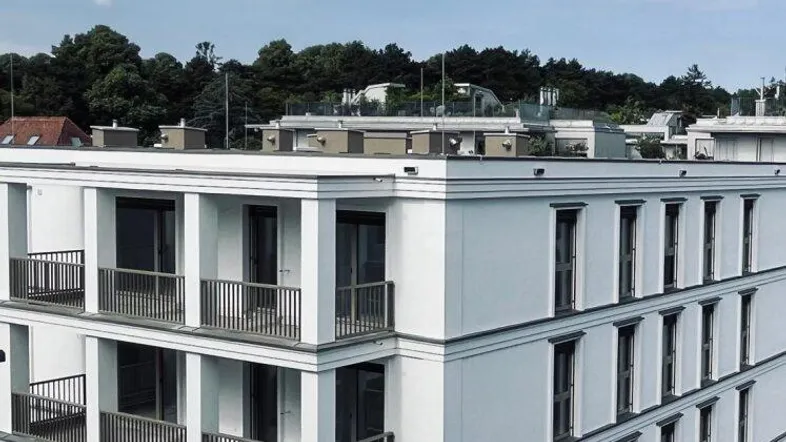 Moderne Wohnanlage mit weißer Fassade und mehreren Balkonen unter blauem Himmel.