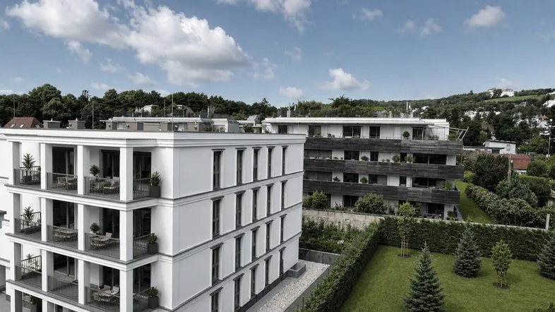 Moderne Wohngebäude mit Balkonen und gepflegter Grünanlage unter blauem Himmel.