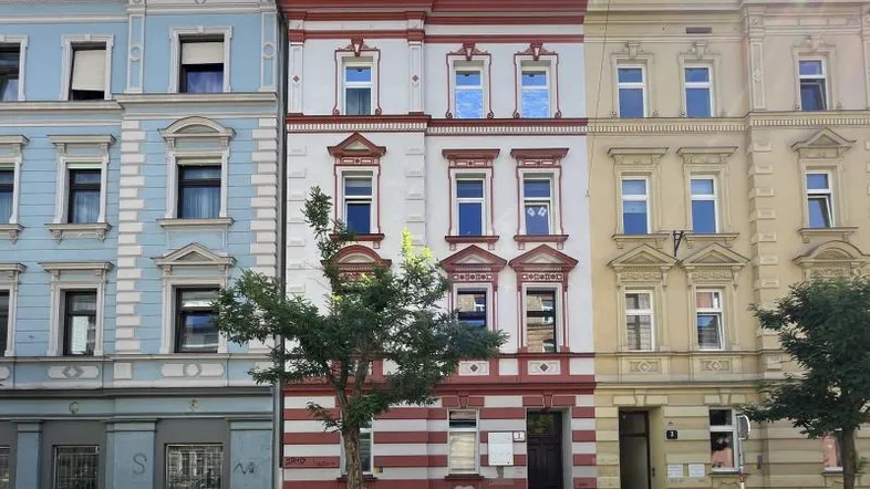 Historische Fassade eines Mehrfamilienhauses mit dekorativen Elementen und großen Fenstern.