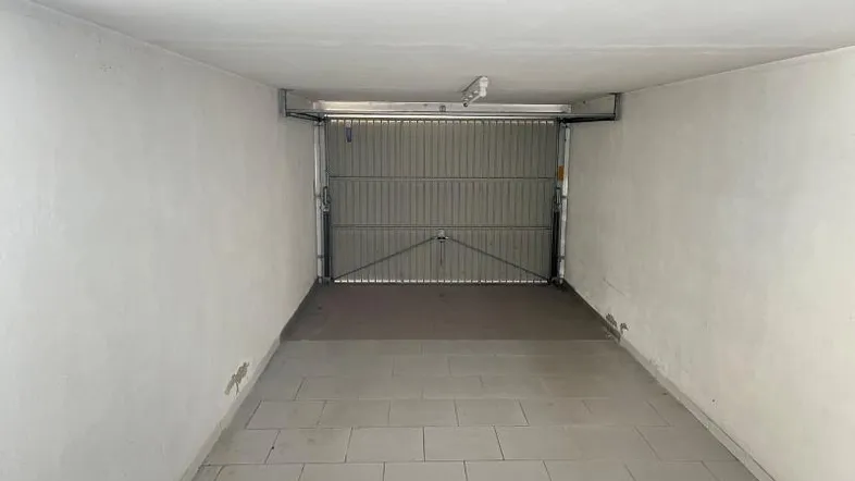 Leere Garage mit Fliesenboden und geöffnetem Rolltor, bereit zur Nutzung.