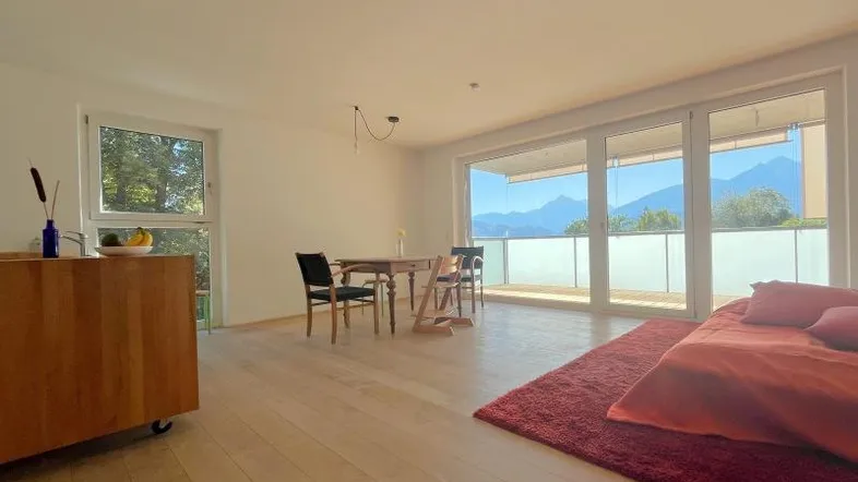 Heller offener Wohn- und Essbereich mit Holzboden, Bergblick und Zugang zum Balkon.