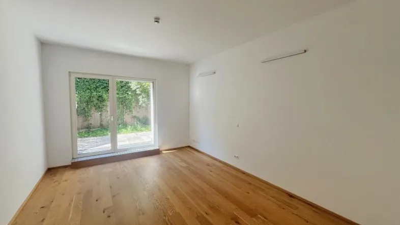 Helles Zimmer mit Holzboden und Zugang zu einer Terrasse oder einem Gartenbereich.