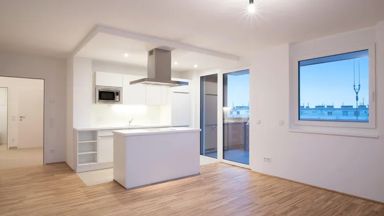 Heller offener Wohn-Essbereich mit moderner Einbauküche, Kochinsel und Zugang zum Balkon.