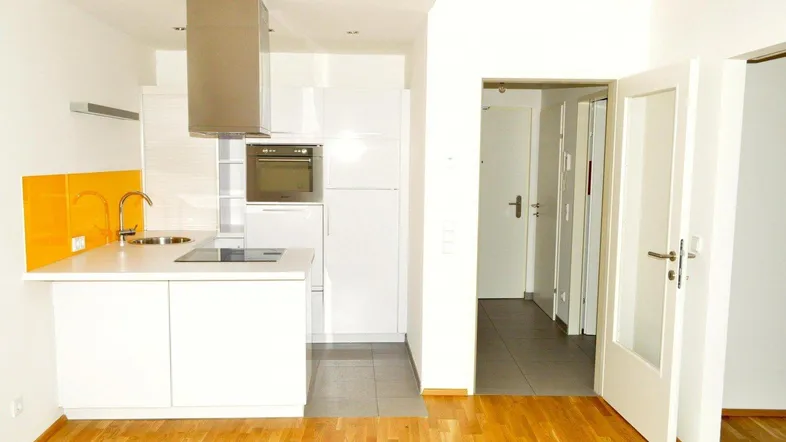 Moderne, helle Küche mit weißen Hochglanzfronten, Kochinsel und Holzboden im angrenzenden Wohnbereich.