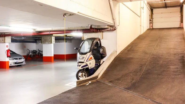 Tiefgaragenzufahrt mit Rampe und Stellplätzen für Fahrzeuge und Fahrräder in einem Gebäude.