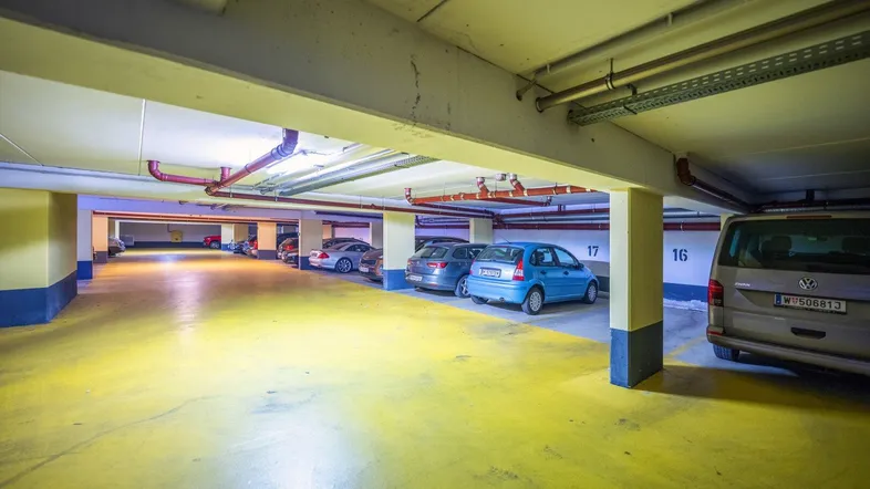 Geräumige Tiefgarage mit mehreren Stellplätzen, gelbem Boden und sichtbaren Installationen.