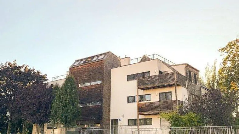 Modernes Mehrfamilienhaus mit Holzfassade und Balkonen, umgeben von Grünflächen.