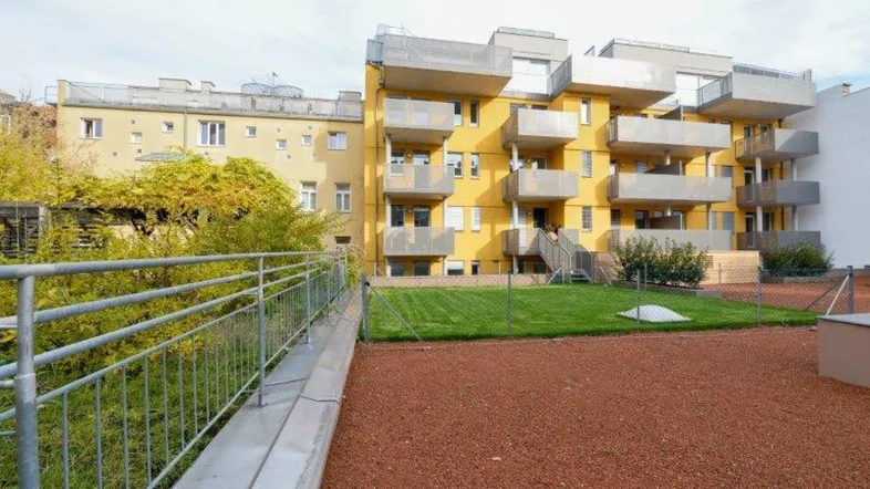 Gelbes Mehrfamilienhaus mit Balkonen und einer kleinen Rasenfläche im Vordergrund.