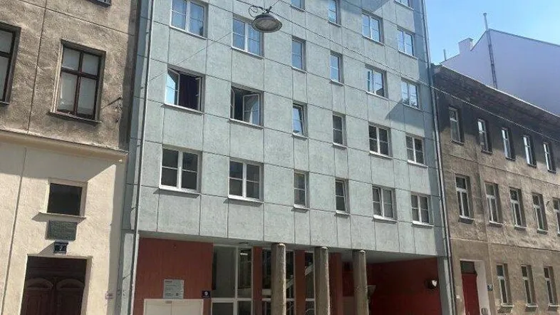 Mehrstöckiges Wohngebäude mit hellblauer Fassade und vielen Fenstern an einer städtischen Straße.