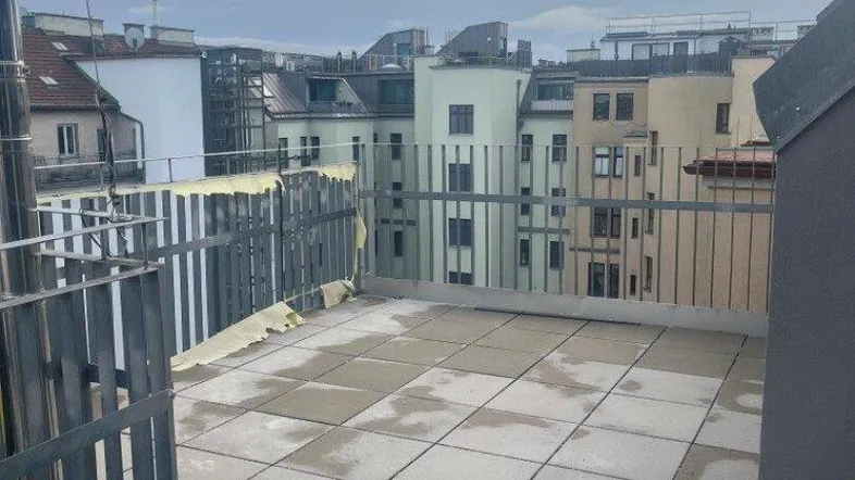 Geräumige Dachterrasse mit Fliesenboden und Metallgeländer, bietet einen weiten Blick über die Stadt.