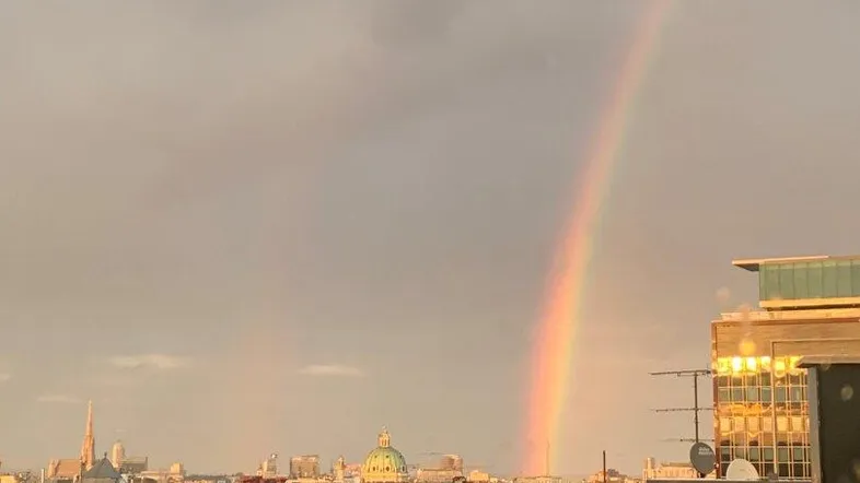 Dachterrasse mit Panoramablick über die Stadt und einem Regenbogen am Himmel.