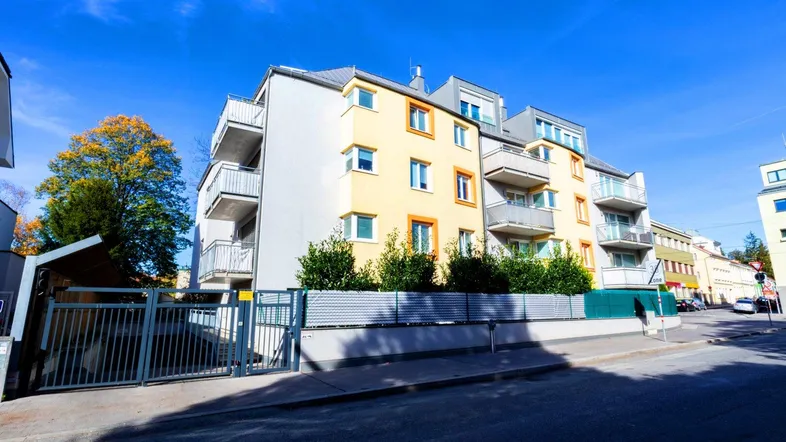 Modernes Mehrfamilienhaus mit gelber Fassade, Balkonen und gepflegter Außenanlage an einer Straße.