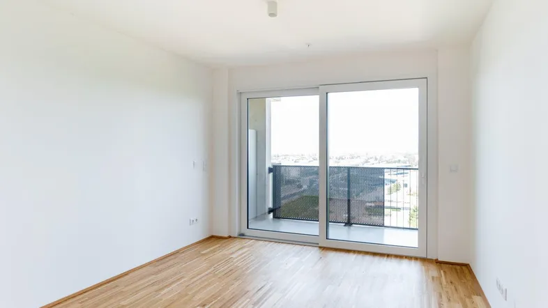 Helles Zimmer mit Holzboden und großem Schiebefenster, das auf einen Balkon führt.
