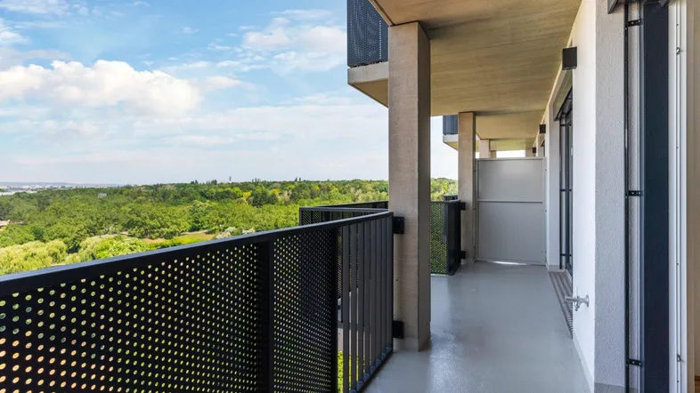 Langer Balkon mit moderner Lochblechbrüstung und weitem Blick ins Grüne und über die Stadt.