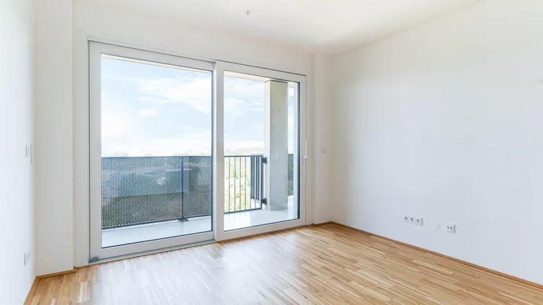 Helles Zimmer mit Holzboden und großen Schiebetüren, die auf einen Balkon führen.