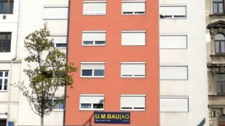 Fassade eines modernen Mehrfamilienhauses mit orangefarbenem Mittelteil und weißen Fensterläden.