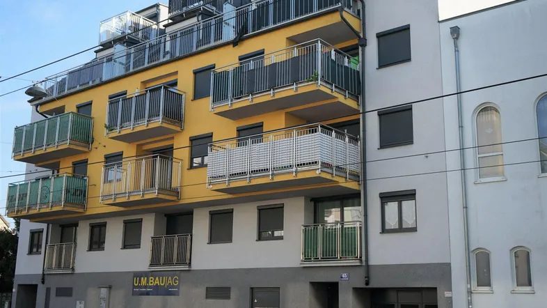 Modernes Mehrfamilienhaus mit gelber Fassade und zahlreichen Balkonen in städtischer Umgebung.
