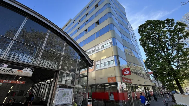 Modernes Geschäftsgebäude mit Glasfassade und U-Bahn-Eingang in städtischer Umgebung.