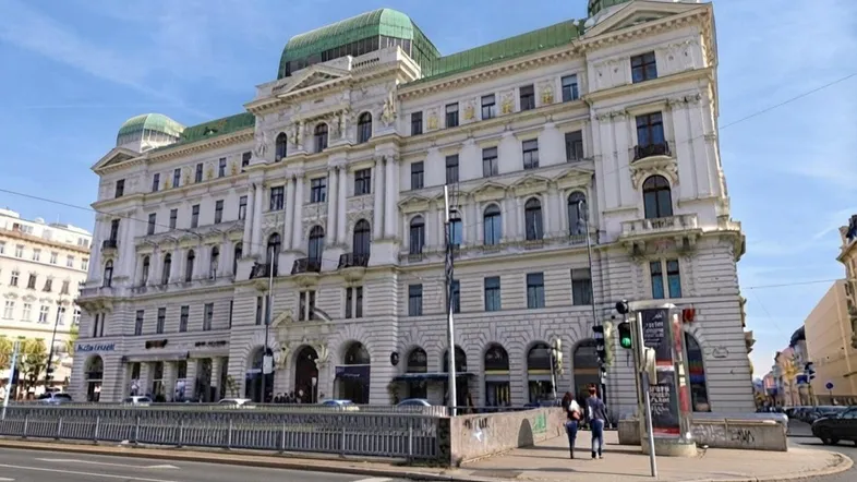 Großes, historisches Gebäude mit klassischer Architektur und grünen Kuppeldächern an einer belebten Straße.