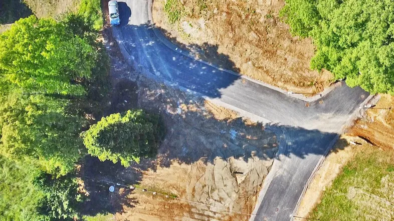 Luftaufnahme einer neu angelegten Straße oder Zufahrt umgeben von viel Grün und Erdboden.