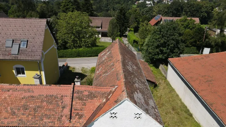 Luftaufnahme von Wohnhäusern mit roten Ziegeldächern und grüner Umgebung, mit Fernblick auf die Stadt.