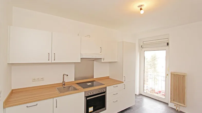 Helle Einbauküche mit weißen Schränken, Holztheke und Zugang zu einem kleinen Balkon.