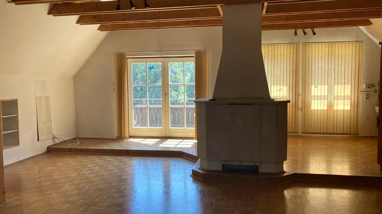 Helles Wohnzimmer mit Holzbalken, Parkettboden, Kamin und Balkonzugang.