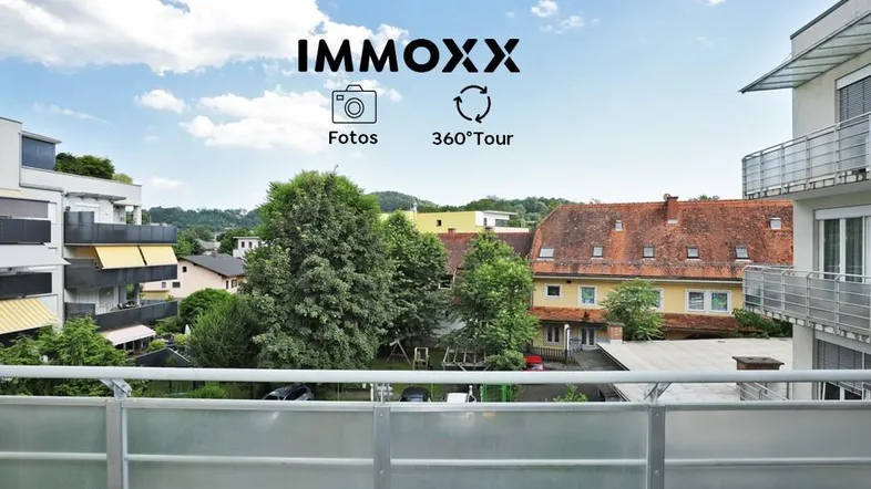 Blick vom Balkon auf die umliegende Wohngegend mit Bäumen und Gebäuden unter blauem Himmel.